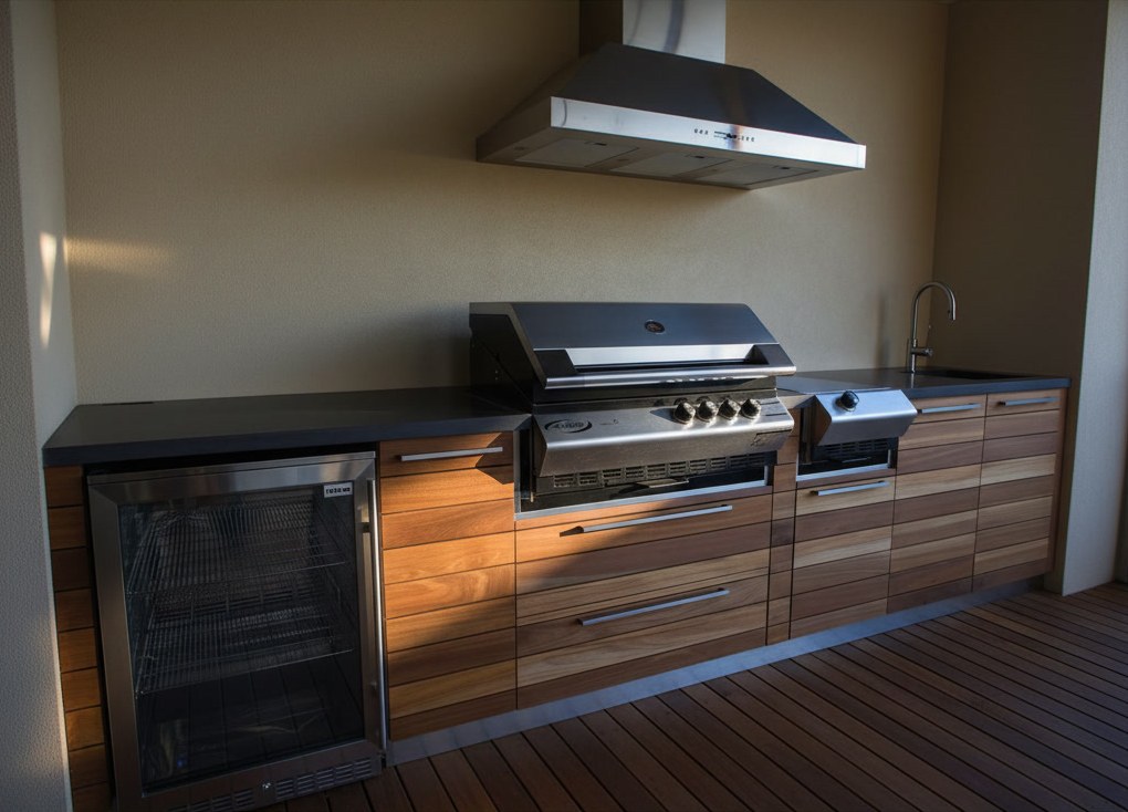 Cucina da esterno lineare con cassetti a doghe di teak, piano scuro, barbecue a gas sotto la cappa in acciaio e cantinetta