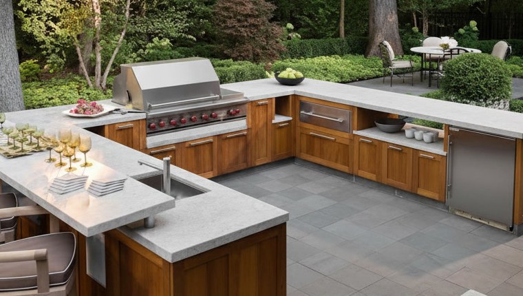 U-shaped outdoor kitchen with a pale granite top on two levels, glasses on the raised ledge, sink and steel barbecue