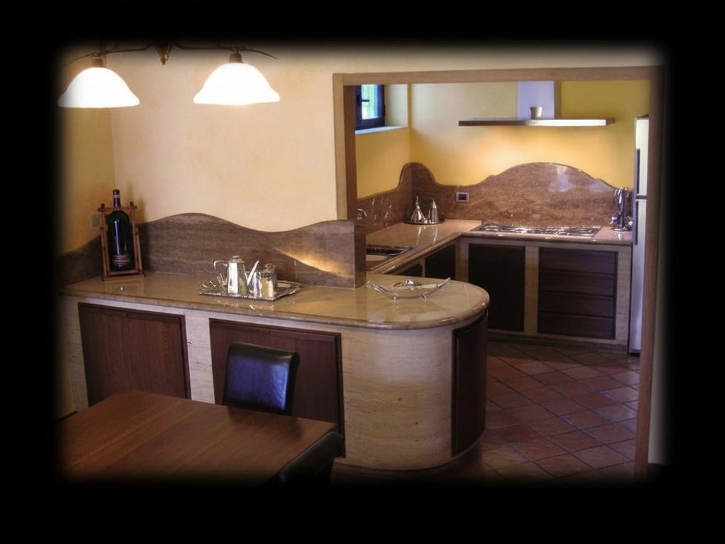 Cucina in muratura con bancone curvo in travertino romano, alzata sagomata in travertino noce e sportelli in noce massello