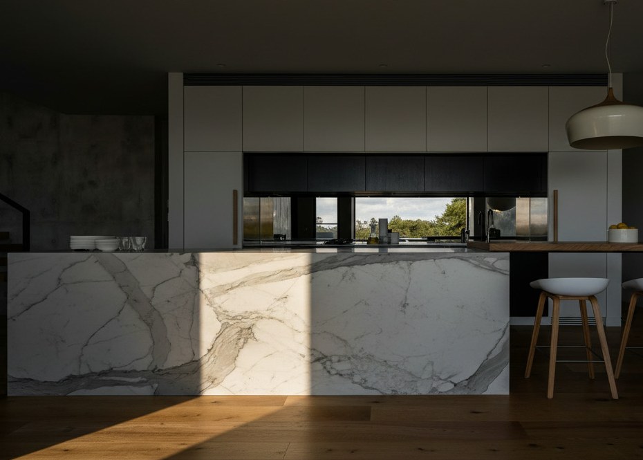 Island in white marble with broad grey veins across its front, timber floor, pale stools and a wall of white cabinets