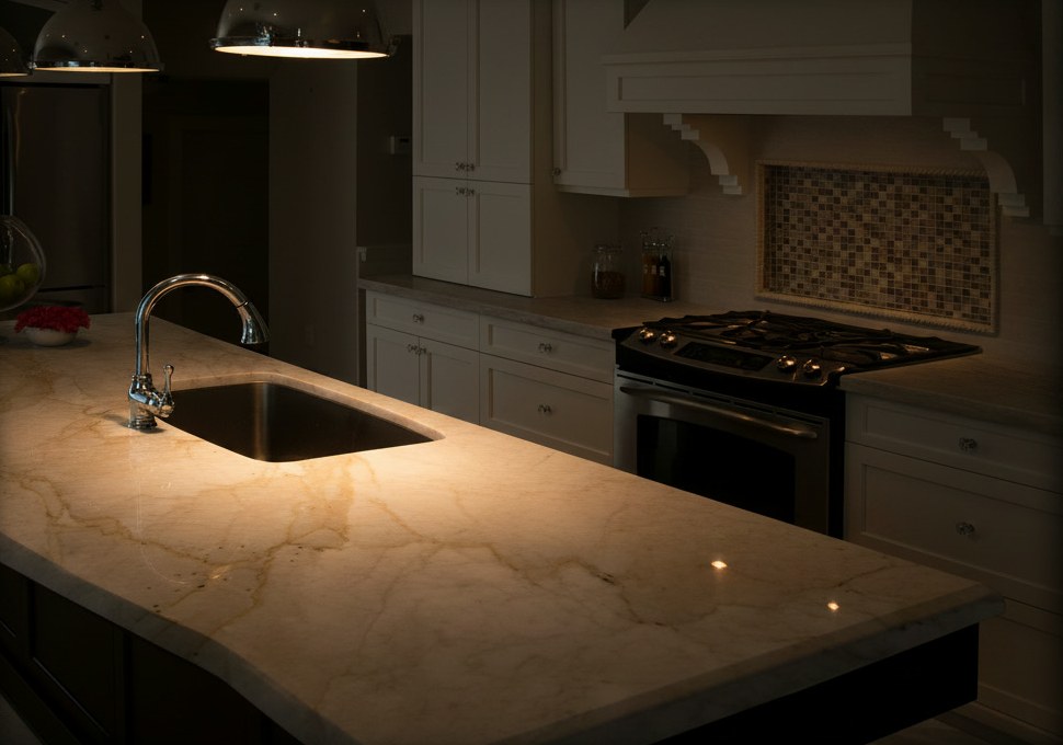 Piano di un'isola in marmo Botticino beige con vene color ocra e lavello sottopiano, in una cucina classica bianca