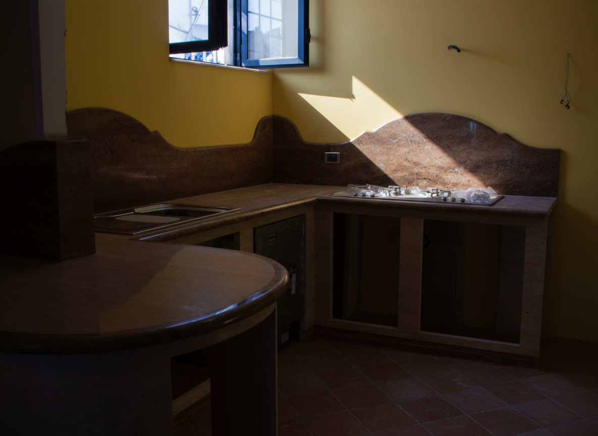 Cucina in muratura in costruzione con alzata sagomata in travertino noce e tavolo rotondo in pietra