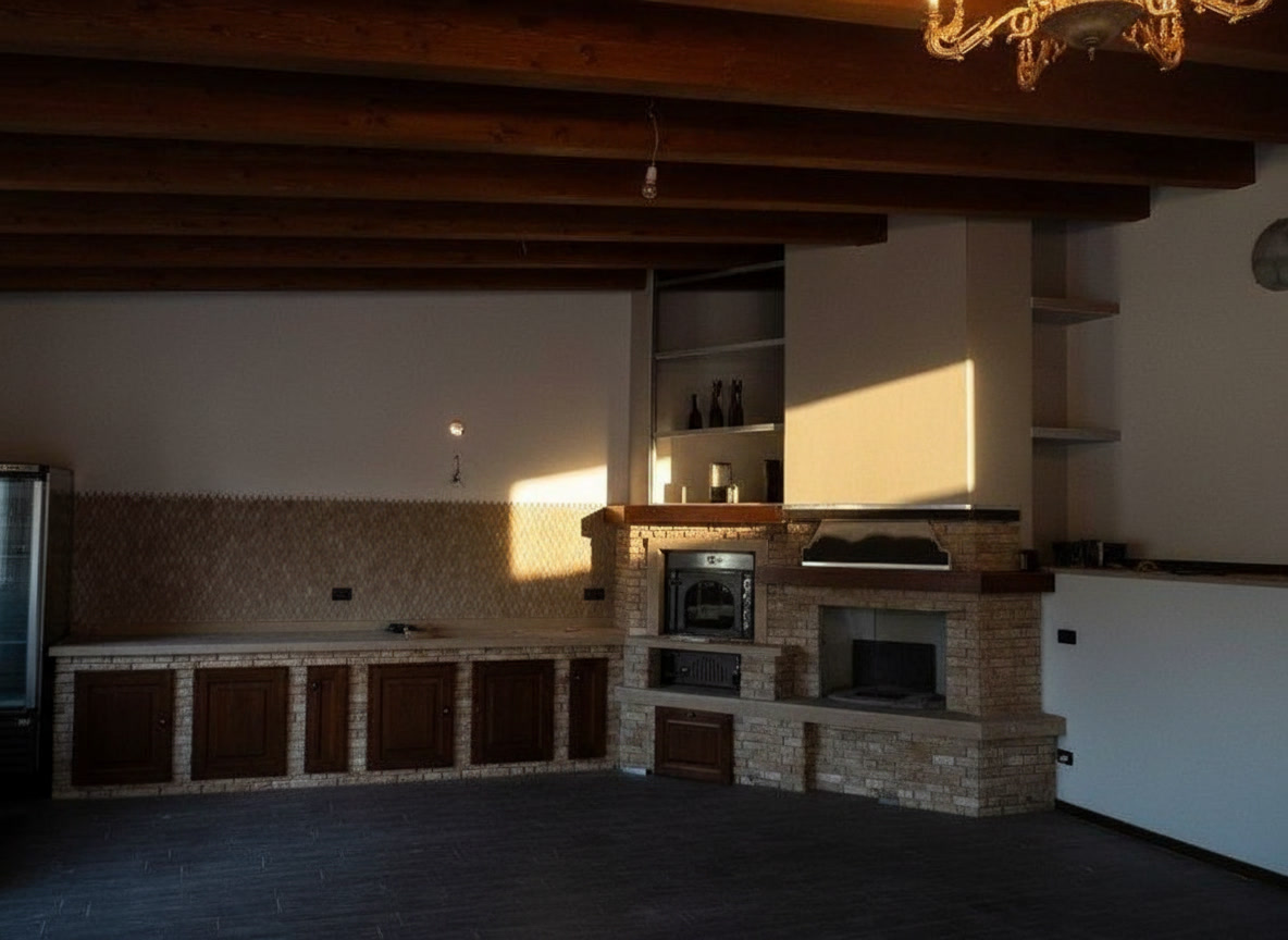 Cucina su misura in muratura finita sotto travi in legno, con forno, camino e lampadario a gocce