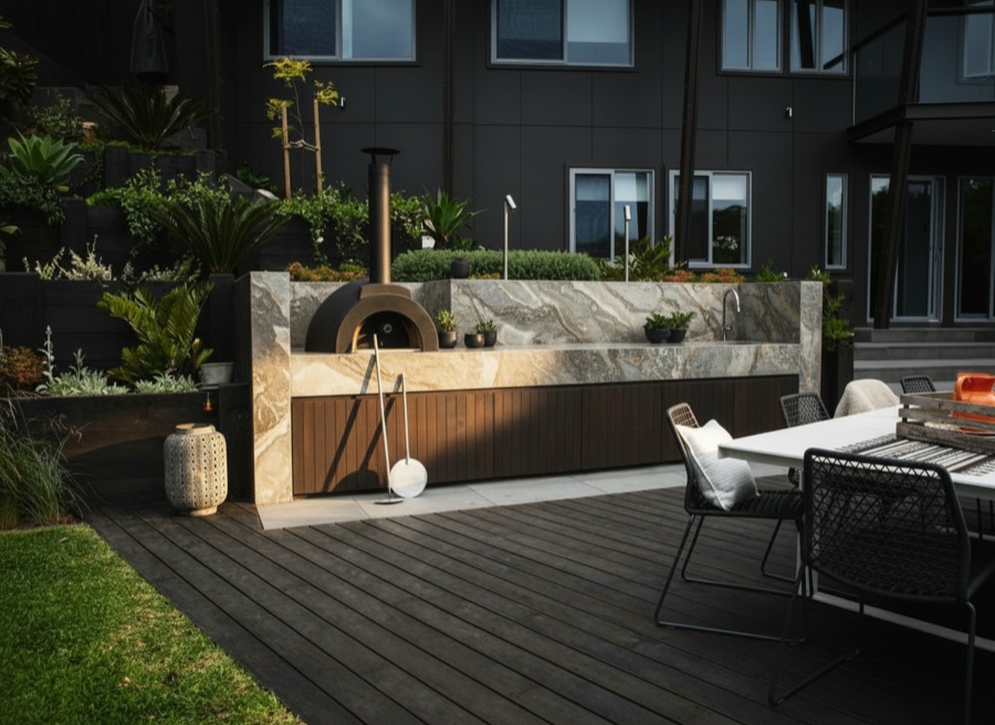 Terrazza con cucina da esterno in pietra e legno scuro, forno per pizza e tavolo da pranzo con sedute