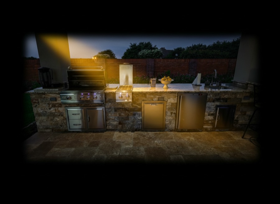 Cucina da esterno rivestita in mattoncini di pietra con lavello, fornelli e barbecue, davanti a un muro in mattoni