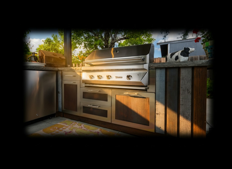 Cucina da esterno con piano in pietra a spacco naturale, ante in legno e acciaio, barbecue a gas incassato