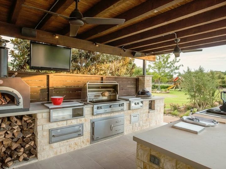 Cucina da esterno in pietra con forno a legna, fornelli, barbecue, isola con lavello e tettoia in legno