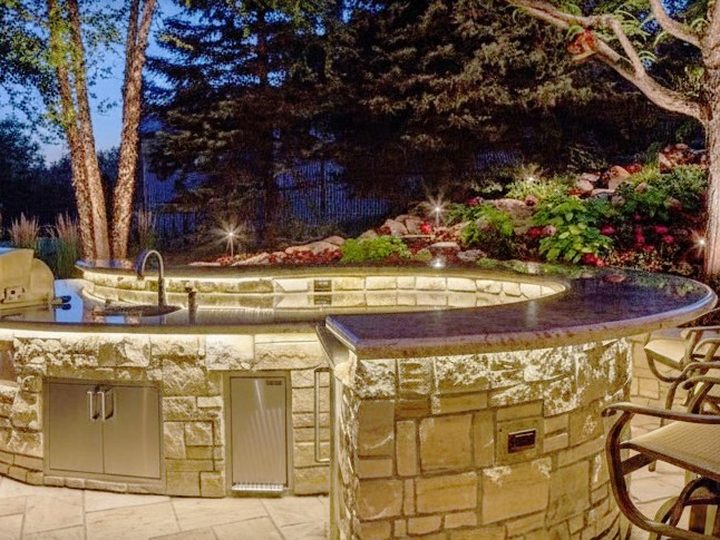 Circular outdoor kitchen in treated marble and granite with professional steel barbecue and night lighting