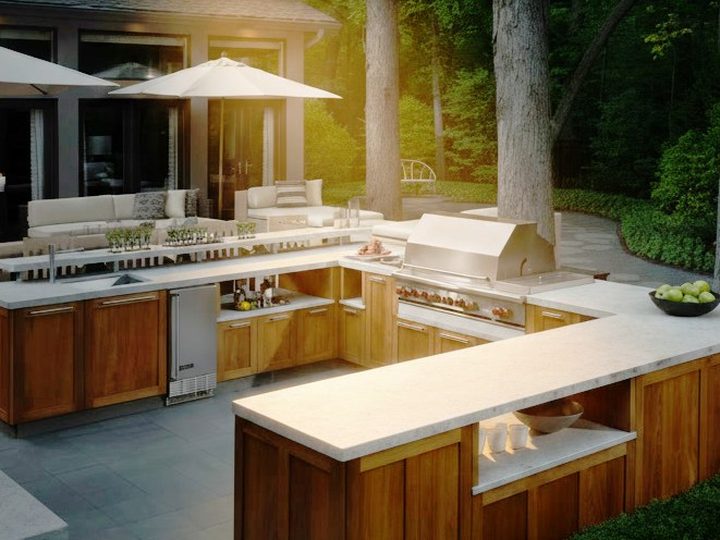 Cucina da esterno moderna a U con piani in marmo chiaro, basi in legno, frigorifero e barbecue da incasso