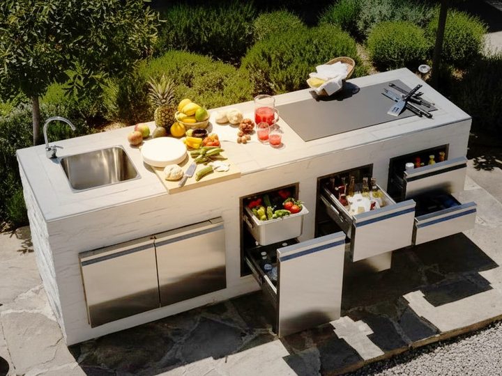 Isola cucina da esterno con lavello, piano di lavoro e dispensa refrigerata a cassetti con verdure fresche