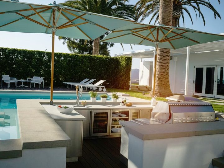 Pianale cucina in pietra e acciaio a bordo piscina con barbecue in acciaio, cantinetta e ombrelloni verde acqua