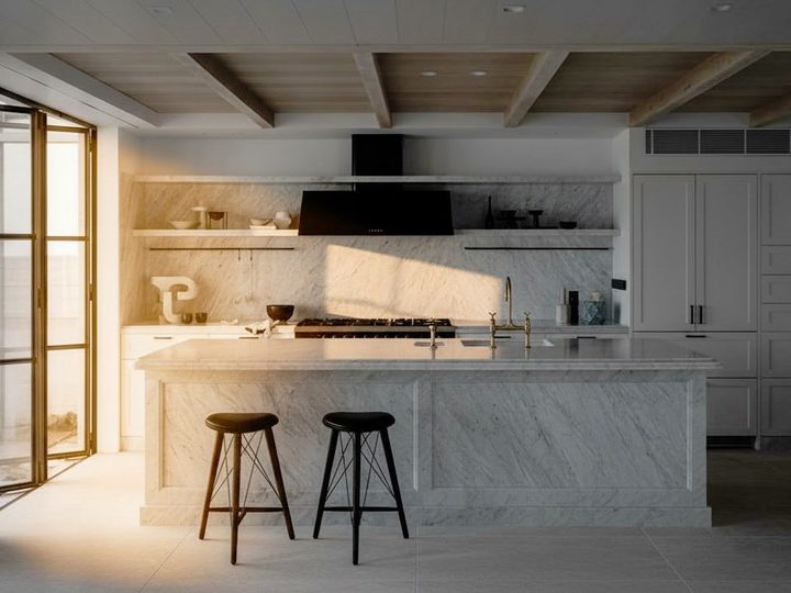 Kitchen with island entirely in Carrara marble, contrasting black hood and dark stools