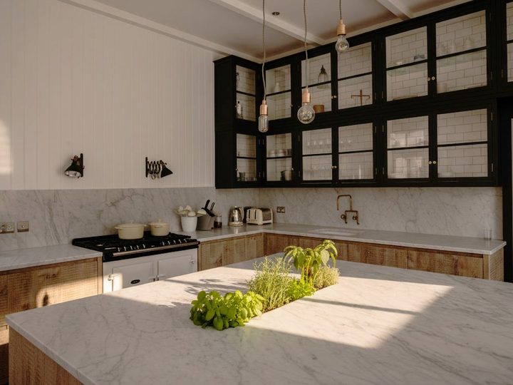 Carrara marble kitchen with contrasting black glass-front cabinets and island with fresh herbs