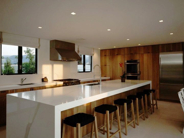 Wooden kitchen with central white table with integrated sink and rows of black stools