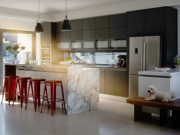 Dark grey lacquered kitchen with veined white marble island, red stools and wooden bench