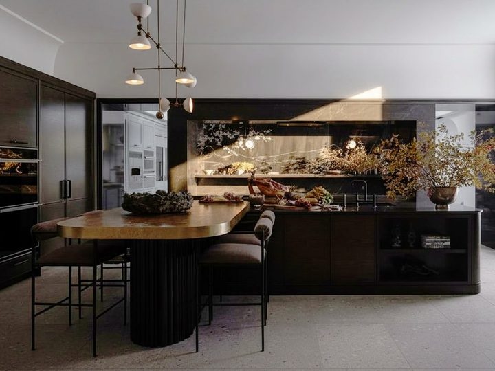 Cucina in legno massello lucido con tavolo ovale, isola con lavello e dettagli in ottone