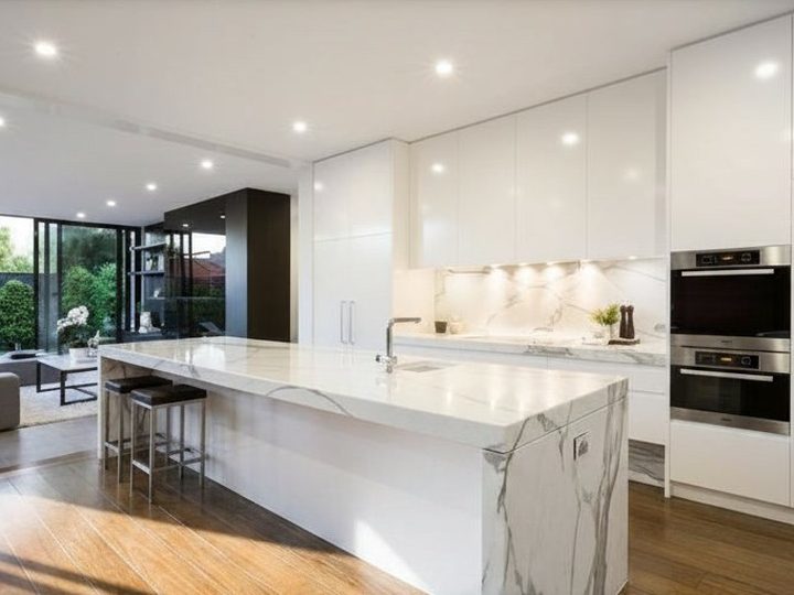 Open space kitchen with white lacquered units and Carrara marble island with waterfall side
