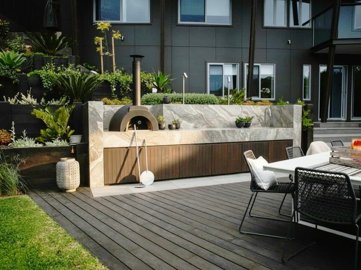 Terrazza con cucina da esterno in pietra e legno scuro, forno per pizza e tavolo da pranzo con sedute