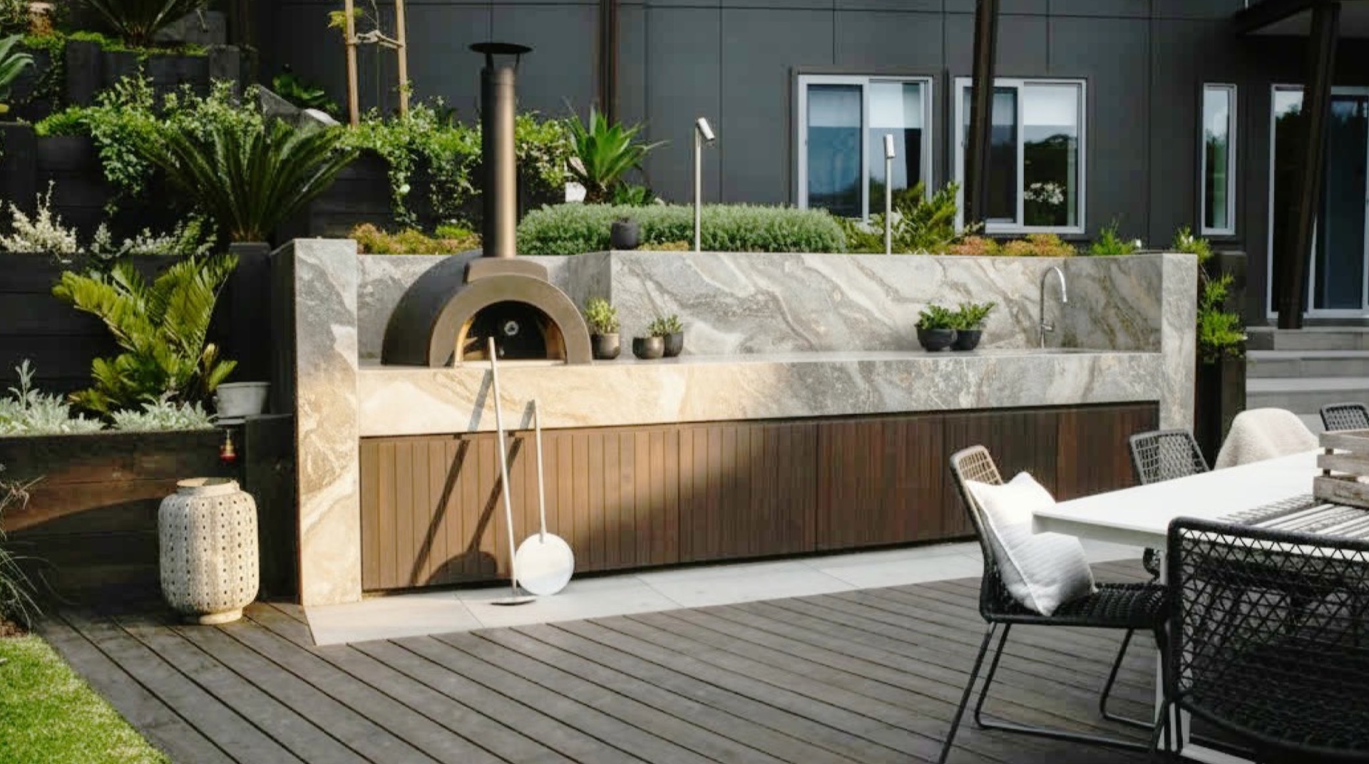 Terrace with stone and dark wood outdoor kitchen, pizza oven and dining table with seating