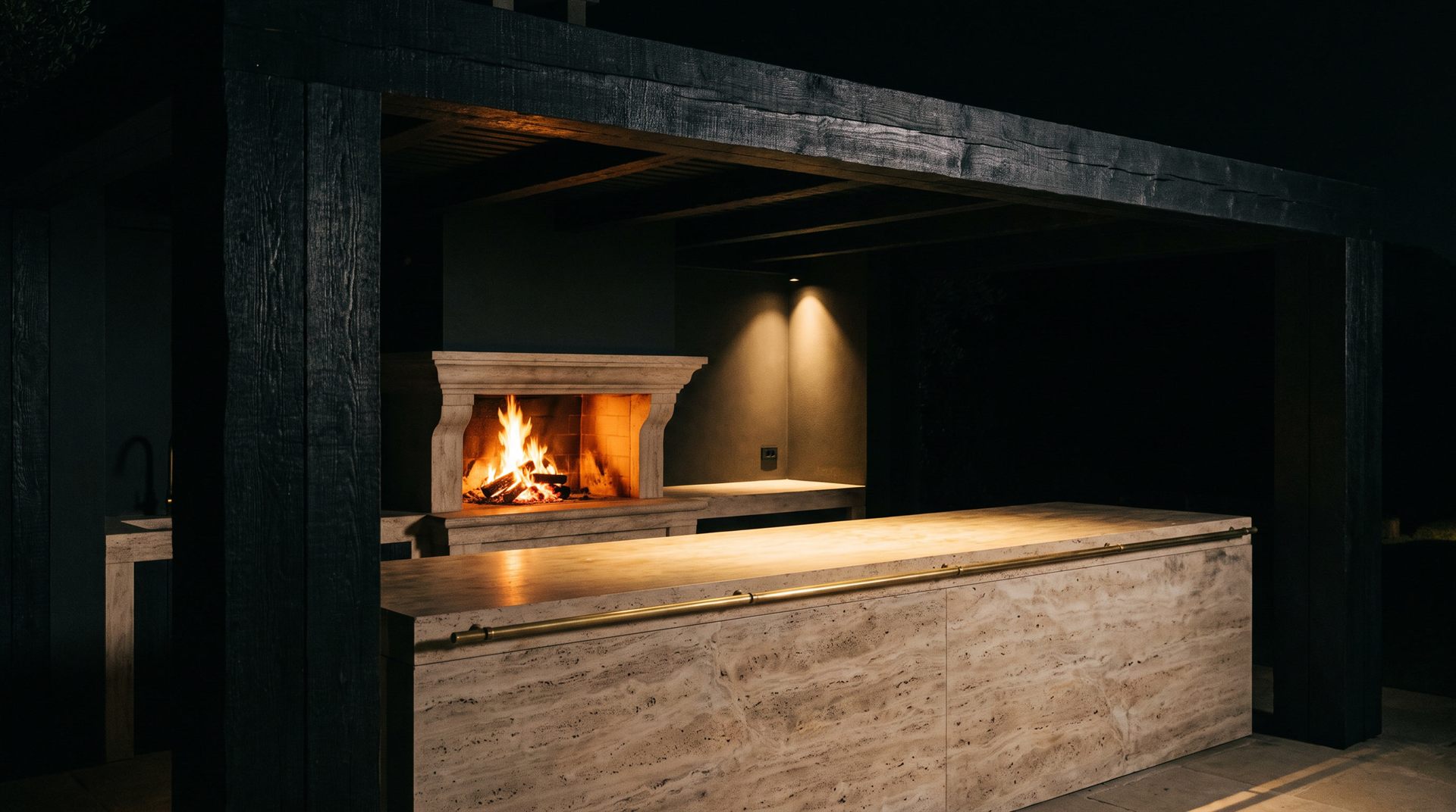 Visione Michelessi: isola in travertino romano con corrimano in ottone sotto un pergolato di legno carbonizzato, camino in pietra acceso nella notte