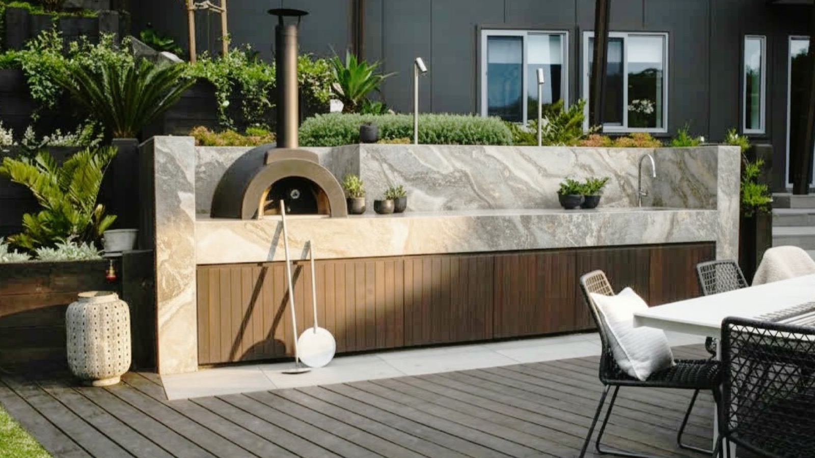 Terrazza con cucina da esterno in pietra e legno scuro, forno per pizza e tavolo da pranzo con sedute