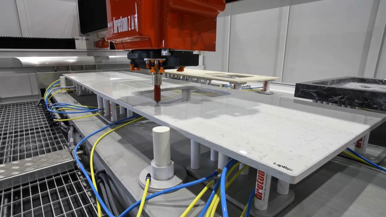 Project vision: the CNC machining centre works a pale slab on its suction supports, with a dark marble bathtub alongside