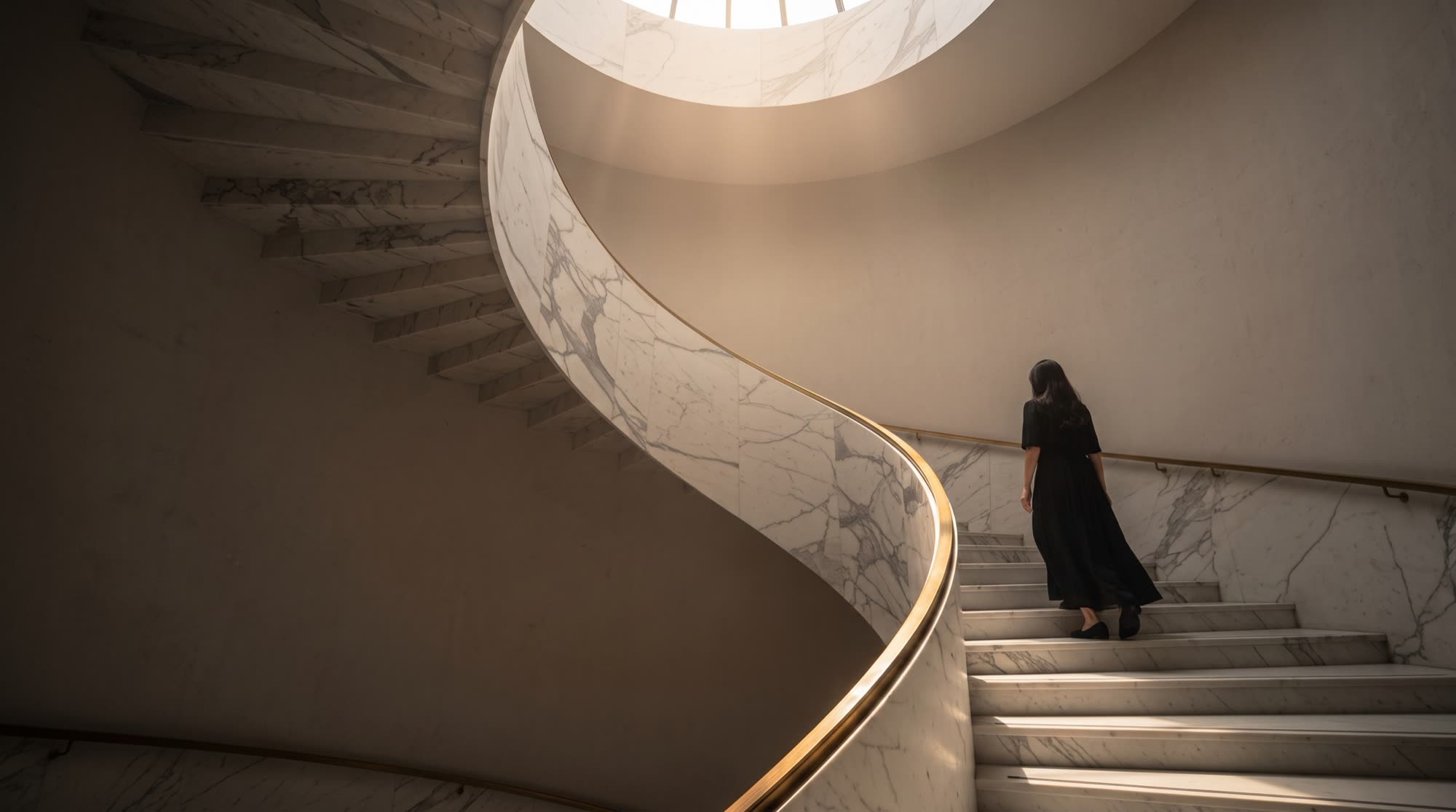 The helicoidal staircase in white statuario marble seen from below, monolithic treads in the dark and a brass handrail lit by the skylight, a Michelessi design vision